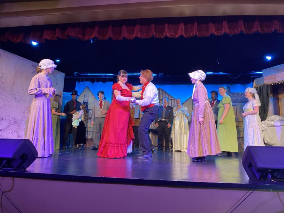 Ashley Merrill (center left in red) as Mrs. Fezziwig and Jim Morgan (center right) as Mr. Fezziwig and the ensemble in A Christmas Carol at Tidewater Players 📷 Sarah O'Hara